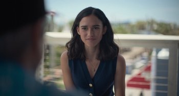 Movie still from “Along for the Ride” (2022), directed by Sofia Alvarez – A woman with long hair is standing in front of a building; Close Up shot, Over the shoulder angle