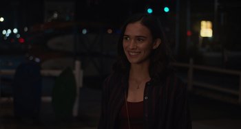 Movie still from “Along for the Ride” (2022), directed by Sofia Alvarez – A young woman smiling for the camera at night; Medium shot, Over the shoulder angle
