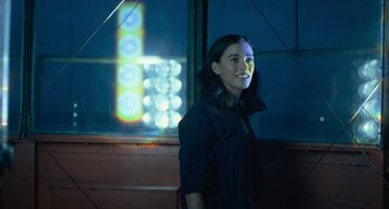 Movie still from “Along for the Ride” (2022), directed by Sofia Alvarez – A woman standing in front of a window at night; Medium shot, Over the shoulder angle
