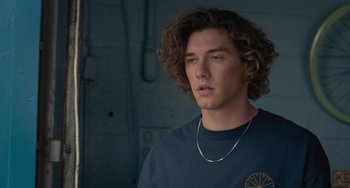 Movie still from “Along for the Ride” (2022), directed by Sofia Alvarez – A young man with long curly hair wearing a blue shirt; Close Up shot, Low angle