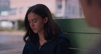 Movie still from “Along for the Ride” (2022), directed by Sofia Alvarez – A woman sitting on top of a wooden bench; Close Up shot, High angle