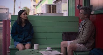 Movie still from “Along for the Ride” (2022), directed by Sofia Alvarez – Two people sitting on a bench with a cup of coffee; Medium shot, Over the shoulder angle