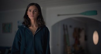 Movie still from “Along for the Ride” (2022), directed by Sofia Alvarez – A young woman standing in a room with her hands in her pockets; Close Up shot, Over the shoulder angle