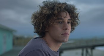 Movie still from “Along for the Ride” (2022), directed by Sofia Alvarez – A person with curly brown hair; Close Up shot, Low angle