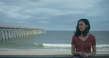 Movie still from “Along for the Ride” (2022), directed by Sofia Alvarez – A woman sitting on a ledge near the ocean; Medium shot, Over the shoulder angle