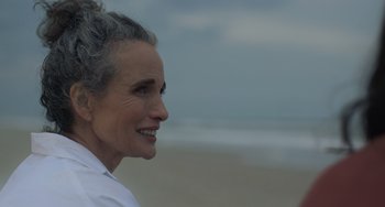 Movie still from “Along for the Ride” (2022), directed by Sofia Alvarez – An older woman standing on the beach looking at the ocean; Close Up shot, Over the shoulder angle