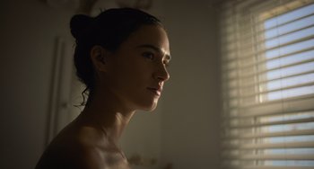 Movie still from “Along for the Ride” (2022), directed by Sofia Alvarez – A beautiful young woman with a bun standing in front of a window; Close Up shot, Low angle