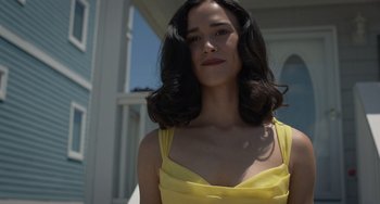 Movie still from “Along for the Ride” (2022), directed by Sofia Alvarez – A woman in a yellow dress standing in front of a building; Close Up shot, Low angle