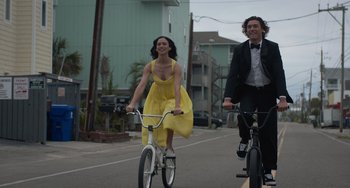 Movie still from “Along for the Ride” (2022), directed by Sofia Alvarez – A man and a woman riding bikes down a street; Medium shot, Low angle