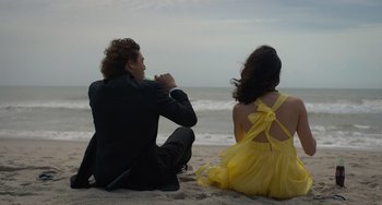 Movie still from “Along for the Ride” (2022), directed by Sofia Alvarez – A man and a woman sitting on the beach; Medium shot, Low angle
