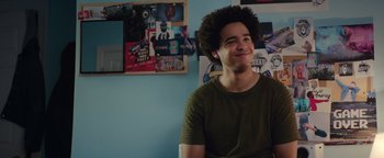 Movie still from “American Carnage” (2022), directed by Diego Hallivis – A young man smiling in front of a blue wall; Close Up shot, Over the shoulder angle