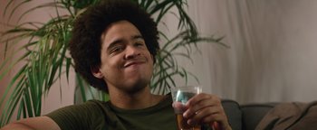 Movie still from “American Carnage” (2022), directed by Diego Hallivis – A young man holding a glass of beer and smiling for the camera; Close Up shot, Over the shoulder angle