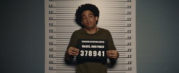 Movie still from “American Carnage” (2022), directed by Diego Hallivis – A man holding up a sign in front of his face; Medium shot, Overhead angle