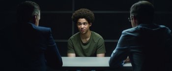 Movie still from “American Carnage” (2022), directed by Diego Hallivis – A man with a very large afro sitting in front of two other men; Medium shot, Over the shoulder angle