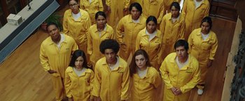 Movie still from “American Carnage” (2022), directed by Diego Hallivis – A group of people standing in yellow suits; Wide shot, High angle