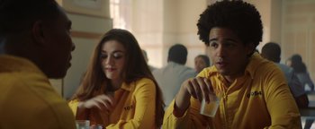 Movie still from “American Carnage” (2022), directed by Diego Hallivis – Two people in yellow shirts are sitting at a table; Medium shot, Over the shoulder angle