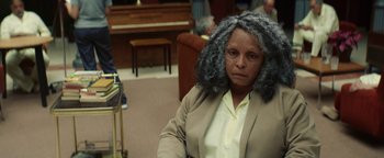 Movie still from “American Carnage” (2022), directed by Diego Hallivis – An older woman sitting in front of a chair; Medium shot, High angle