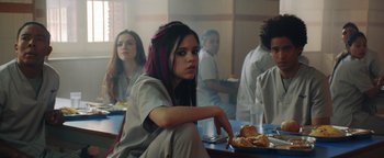 Movie still from “American Carnage” (2022), directed by Diego Hallivis – A woman sitting in front of a table with food on top of it; Medium shot, Over the shoulder angle