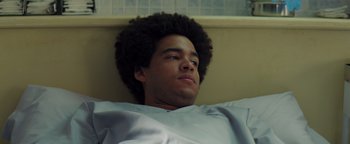 Movie still from “American Carnage” (2022), directed by Diego Hallivis – A young man with a large afro is laying in a hospital bed; Close Up shot, Low angle