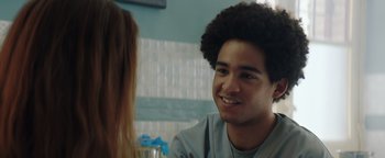 Movie still from “American Carnage” (2022), directed by Diego Hallivis – A young man smiling at a woman in a room with blue walls; Close Up shot, Over the shoulder angle