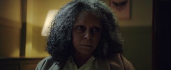 Movie still from “American Carnage” (2022), directed by Diego Hallivis – An older woman with a very long curly hair; Close Up shot, Over the shoulder angle