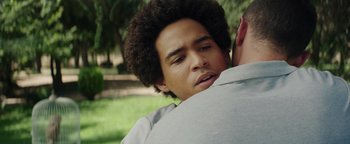Movie still from “American Carnage” (2022), directed by Diego Hallivis – A young man is hugging another man in a park; Close Up shot, Over the shoulder angle