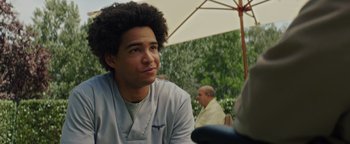 Movie still from “American Carnage” (2022), directed by Diego Hallivis – A man with a curly hair sitting under an umbrella; Close Up shot, Low angle