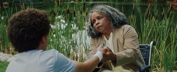 Movie still from “American Carnage” (2022), directed by Diego Hallivis – An older woman sitting down holding hands with another person; Close Up shot, Over the shoulder angle