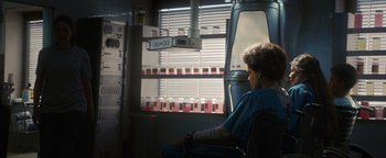 Movie still from “American Carnage” (2022), directed by Diego Hallivis – A woman sitting in a chair looking out a window; Medium shot, Over the shoulder angle