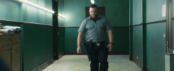 Movie still from “American Carnage” (2022), directed by Diego Hallivis – A man in a police uniform holding a gun in a hallway; Medium shot, Low angle