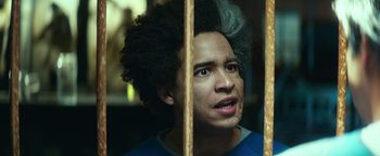 Movie still from “American Carnage” (2022), directed by Diego Hallivis – A young man with curly black hair looking out of a jail cell; Close Up shot, Low angle