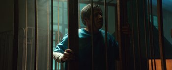 Movie still from “American Carnage” (2022), directed by Diego Hallivis – A man standing behind bars in a jail cell; Medium shot, Low angle
