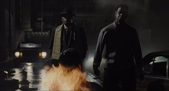 Movie still from “American Gangster” (2007), directed by Ridley Scott – A group of men standing next to each other near a fire; Medium shot, Over the shoulder angle