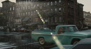 Movie still from “American Gangster” (2007), directed by Ridley Scott – A truck driving down a street next to a building; Wide shot, High angle