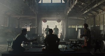 Movie still from “American Gangster” (2007), directed by Ridley Scott – A group of people sitting in a room; Extreme Wide shot, Low angle