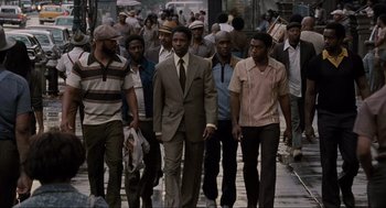 Movie still from “American Gangster” (2007), directed by Ridley Scott – A group of people walking down a street; Wide shot, Low angle