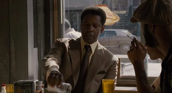 Movie still from “American Gangster” (2007), directed by Ridley Scott – A man sitting at a table in a suit and tie; Medium shot, Over the shoulder angle