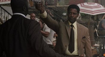 Movie still from “American Gangster” (2007), directed by Ridley Scott – A man in a suit and tie holding a gun in his hand; Medium shot, Low angle
