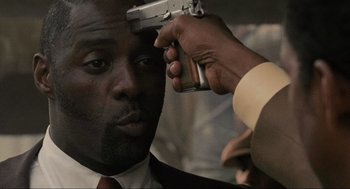 Movie still from “American Gangster” (2007), directed by Ridley Scott – A man in a suit and tie holding a gun up to his face; Close Up shot, High angle