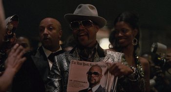 Movie still from “American Gangster” (2007), directed by Ridley Scott – A man holding up a magazine in front of two other people; Close Up shot, Overhead angle