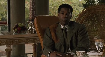 Movie still from “American Gangster” (2007), directed by Ridley Scott – A man sitting in a chair in front of a table; Medium shot, Over the shoulder angle