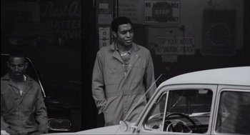 Movie still from “American Gangster” (2007), directed by Ridley Scott – A black and white photo of a man standing in front of a car; Medium shot, Low angle