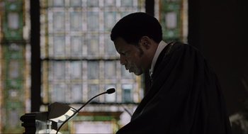 Movie still from “American Gangster” (2007), directed by Ridley Scott – A man in a robe is speaking into a microphone; Close Up shot, Low angle