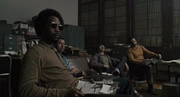 Movie still from “American Gangster” (2007), directed by Ridley Scott – A group of men sitting on a couch in front of a window; Medium shot, Low angle