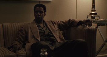 Movie still from “American Gangster” (2007), directed by Ridley Scott – A man sitting on top of a couch next to a wine glass; Medium shot, Low angle