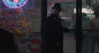 Movie still from “American Gangster” (2007), directed by Ridley Scott – A man wearing a hat standing in front of a christmas tree; Medium shot, Over the shoulder angle