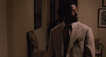 Movie still from “American Gangster” (2007), directed by Ridley Scott – A man wearing a suit and tie in a room; Medium shot, Over the shoulder angle