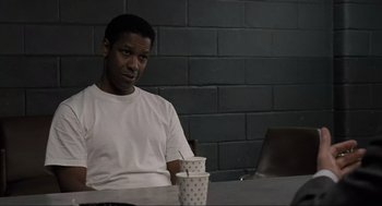Movie still from “American Gangster” (2007), directed by Ridley Scott – A man sitting at a table with two cups in front of him; Medium shot, Over the shoulder angle