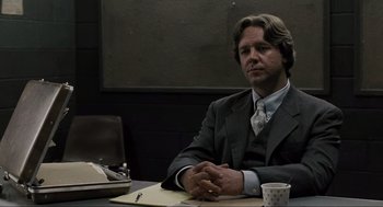 Movie still from “American Gangster” (2007), directed by Ridley Scott – A man sitting at a table in a suit and tie; Medium shot, Over the shoulder angle