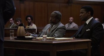 Movie still from “American Gangster” (2007), directed by Ridley Scott – A group of men sitting at a table in a courtroom; Medium shot, Over the shoulder angle